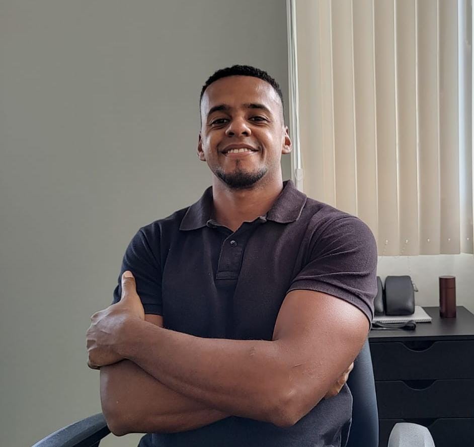Dr. Raphael Nunes, fisioterapeuta da equipe EARFF, homem sorrindo de braços cruzados vestindo polo escura em consultório clínico moderno, fotografia realista