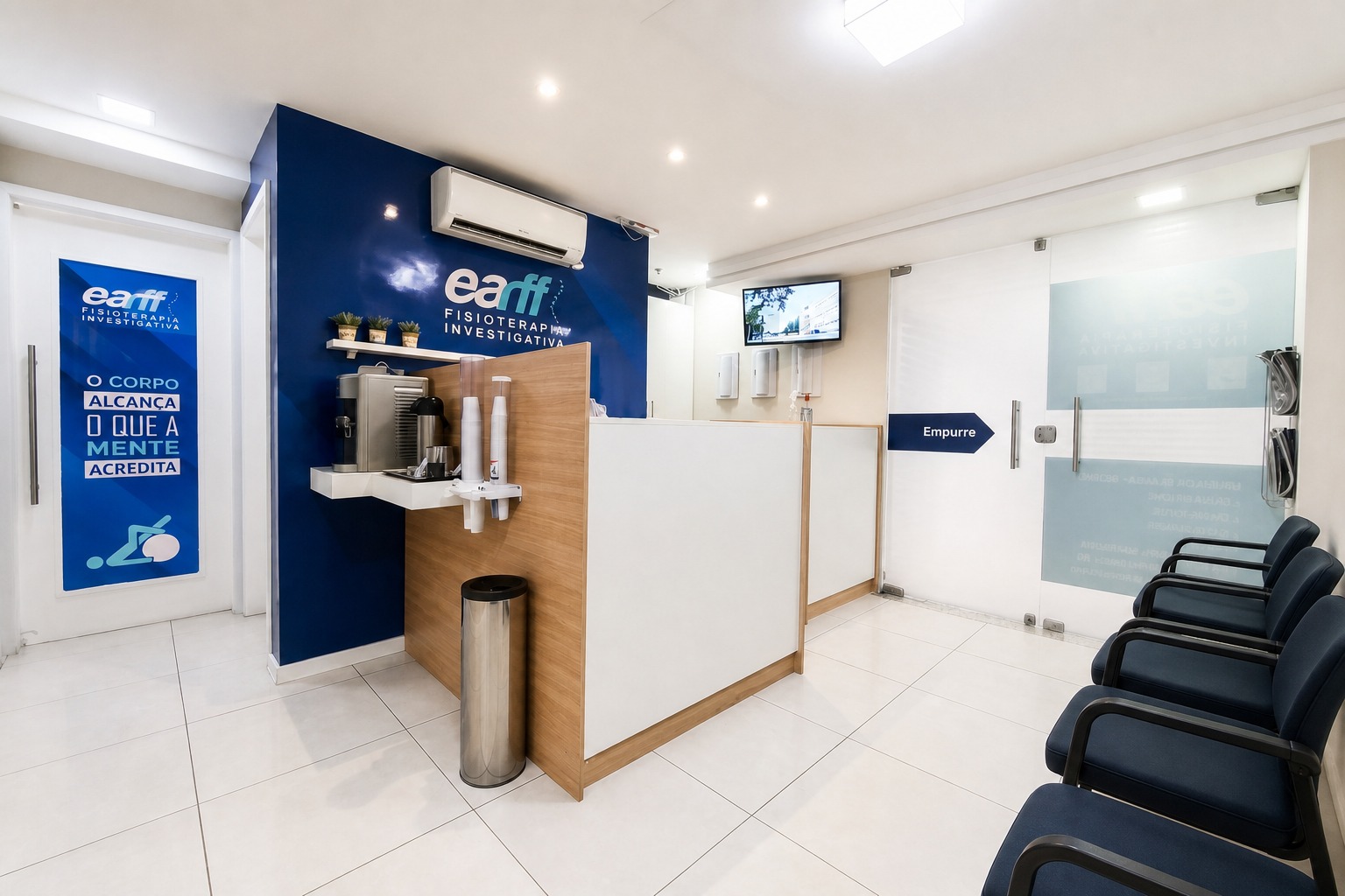 Recepção da unidade EARFF Niterói, balcão de madeira com pia e utensílios de café, parede azul-marinho com logo EARFF, cadeiras de espera azuis, piso branco, ambiente clínico moderno e clean, fotografia realista